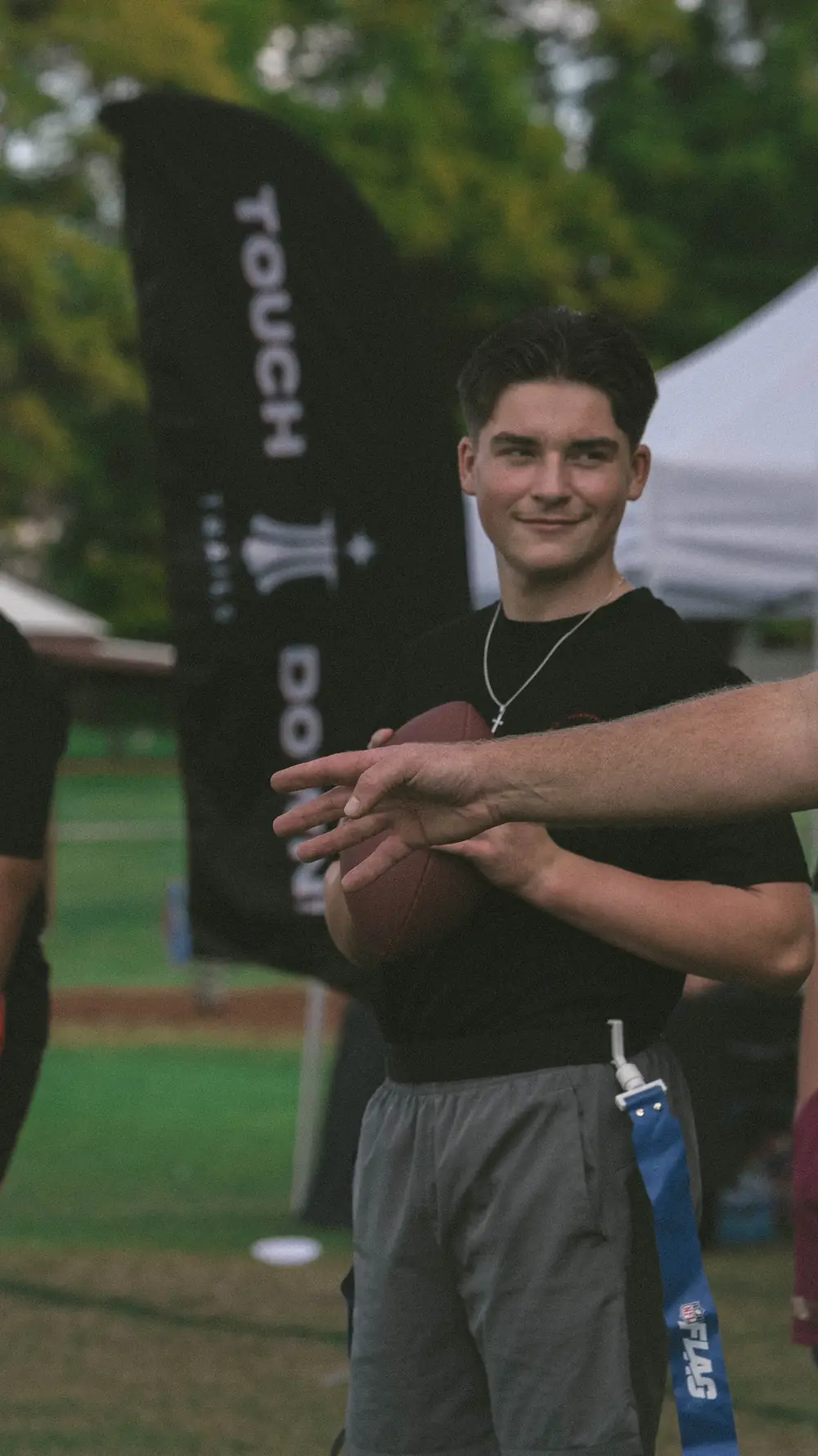 A young player holding a football on the field, the Touchdown banner behind him